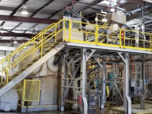Mill equipment with a raised platform and yellow safety rails.