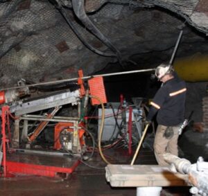 A worker beside underground diamond drilling equipment.