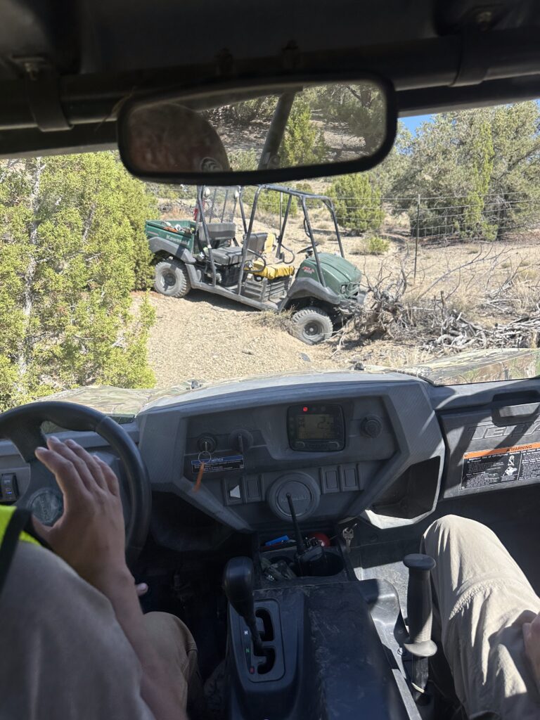 An off-road utility vehicle beside a field track, viewed from another vehicle.
